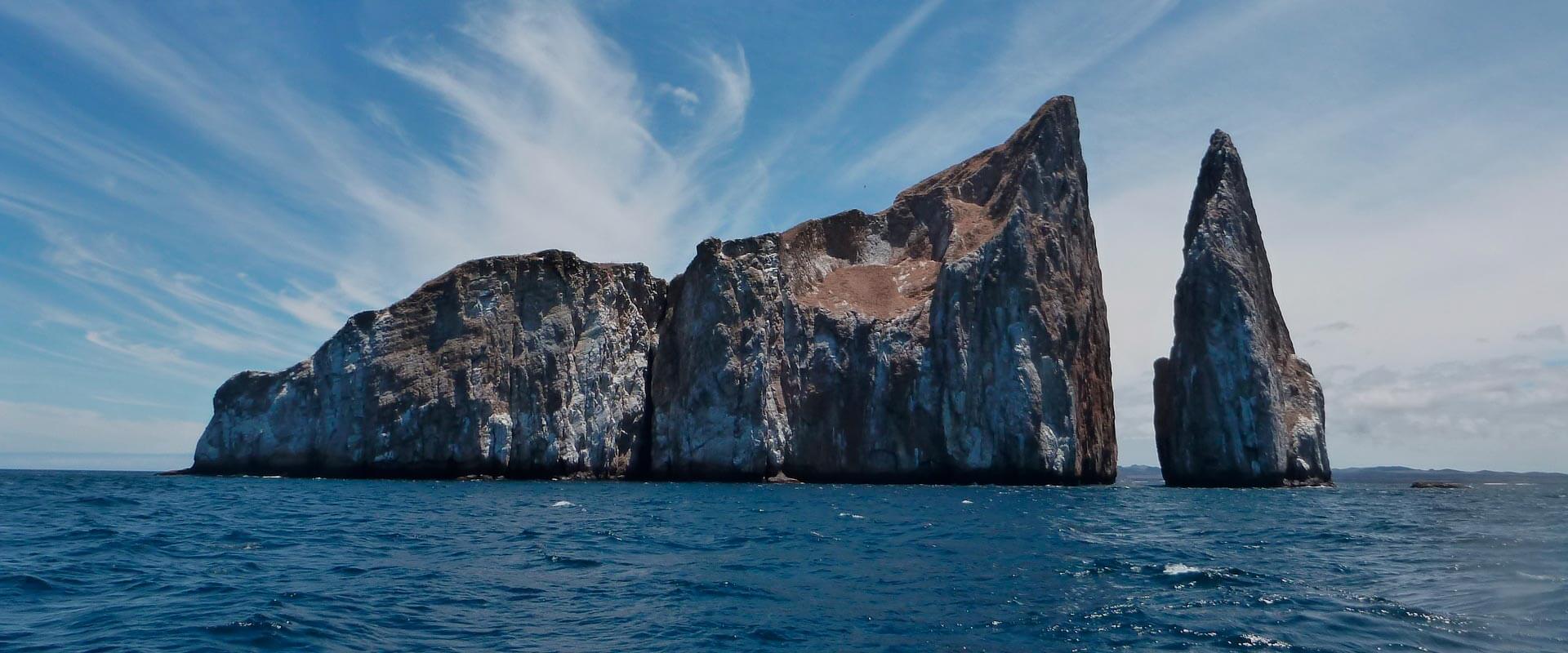 Tall rocky sea stacks rising from blue ocean water under a bright sky with wispy clouds, calm and expansive